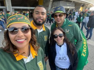A group of smiling travellers wearing Springboks and All Blacks rugby jerseys taking a selfie outside a stadium during a DBD Travel group tour.