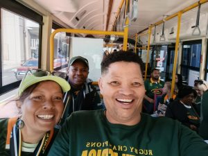 Smiling travellers wearing Springboks rugby shirts taking a selfie on a DBD Travel group tour bus